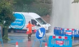 泰晤士水务公司的一名员工拼命地把锥筒放在水管破裂后30英尺高的水柱周围